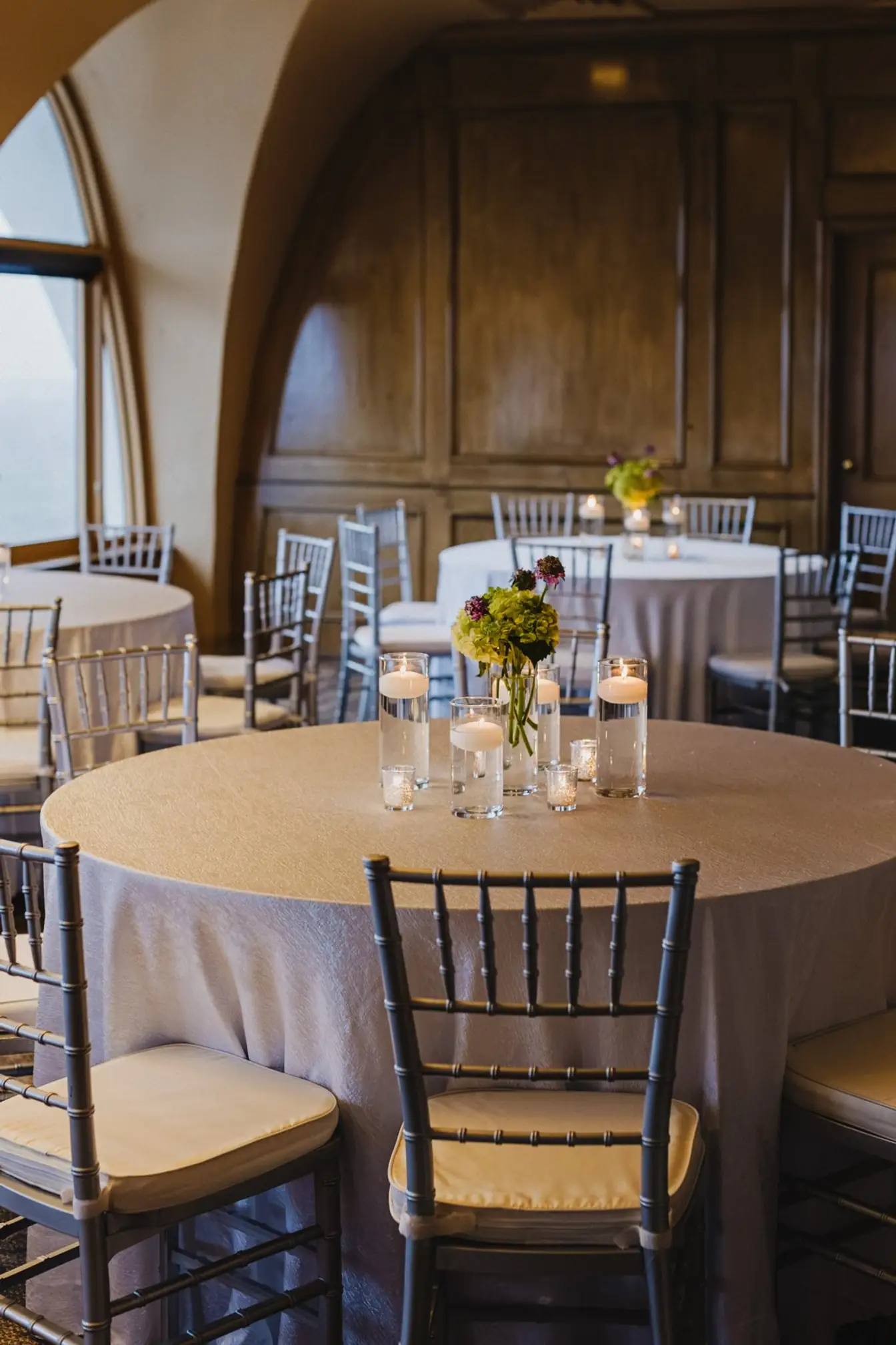 Round table in a shimmering ivory crushed floor-length linen with silver Chiavari chairs and floating-candle centerpieces — linen rentals from Party Connection Memphis