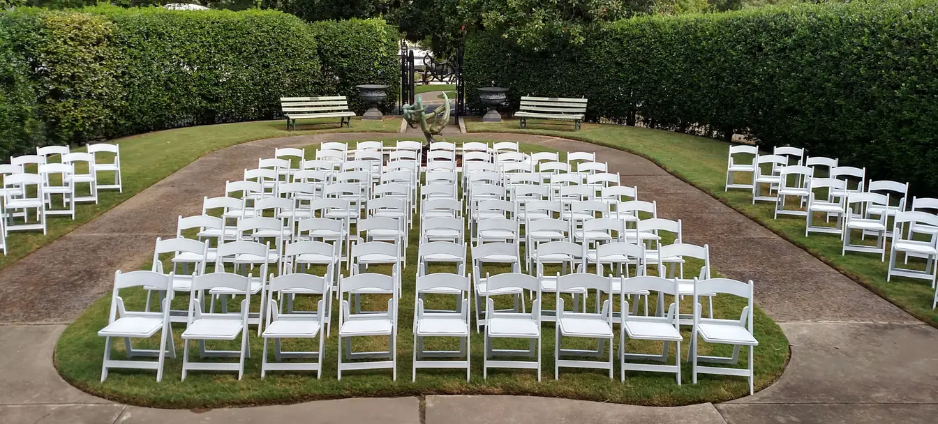 Rows of white resin folding chairs set for a garden ceremony in Memphis