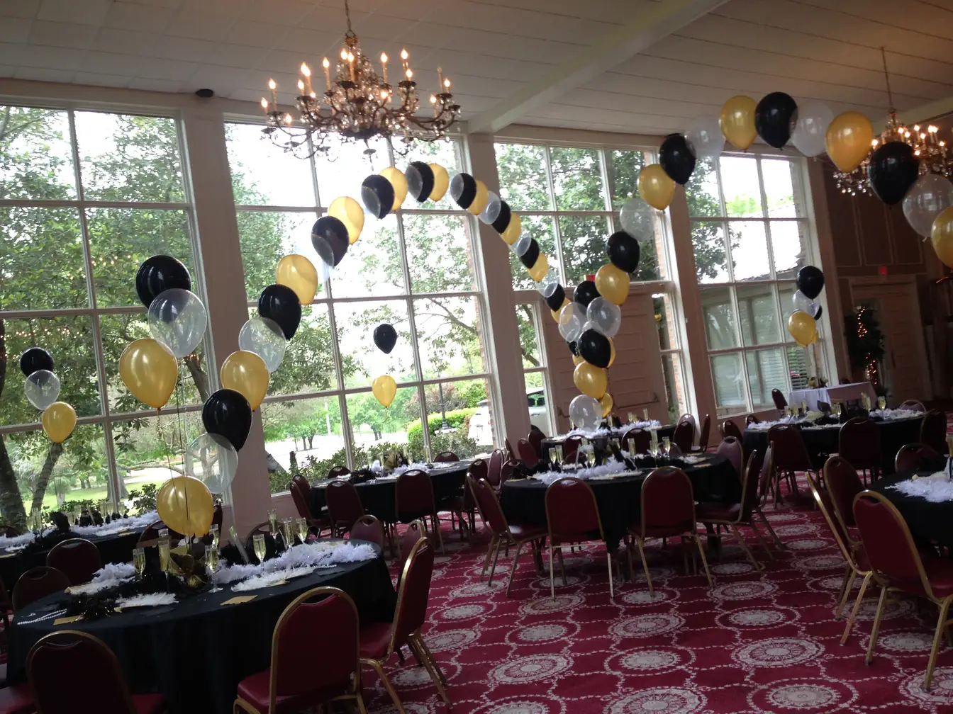 Gold and black balloons gathered under a chandelier in a windowed hall