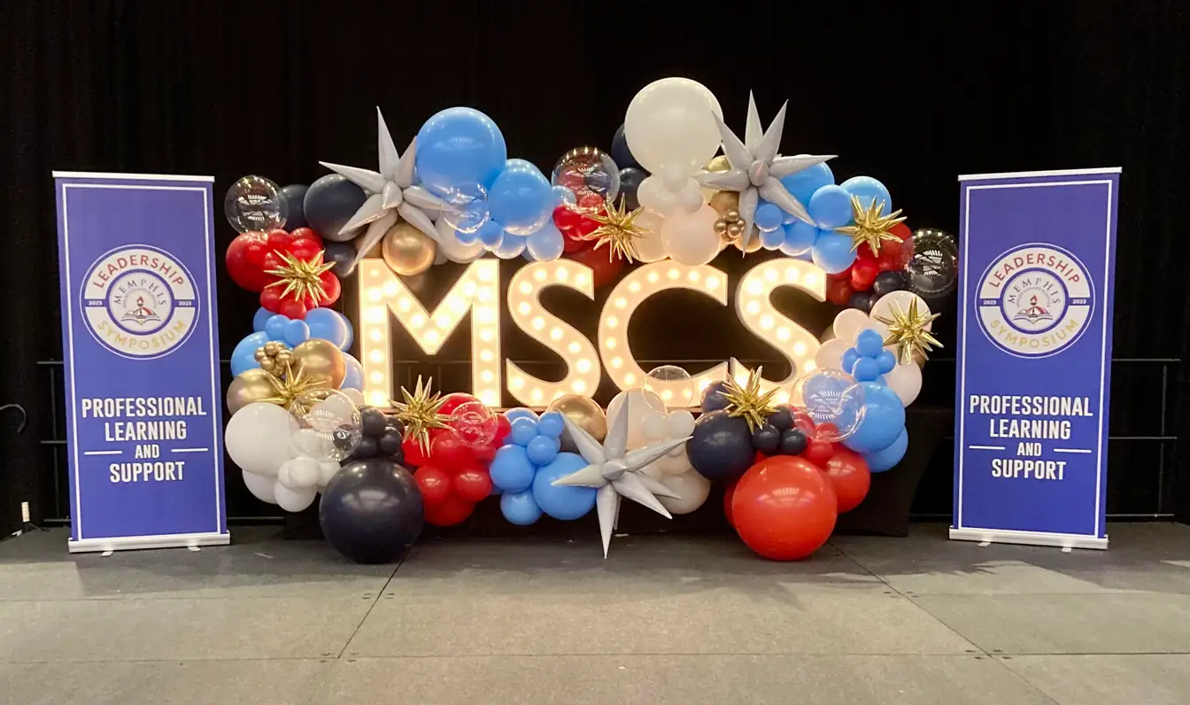 Organic balloon installation in red, blue, and gold around lighted marquee letters
