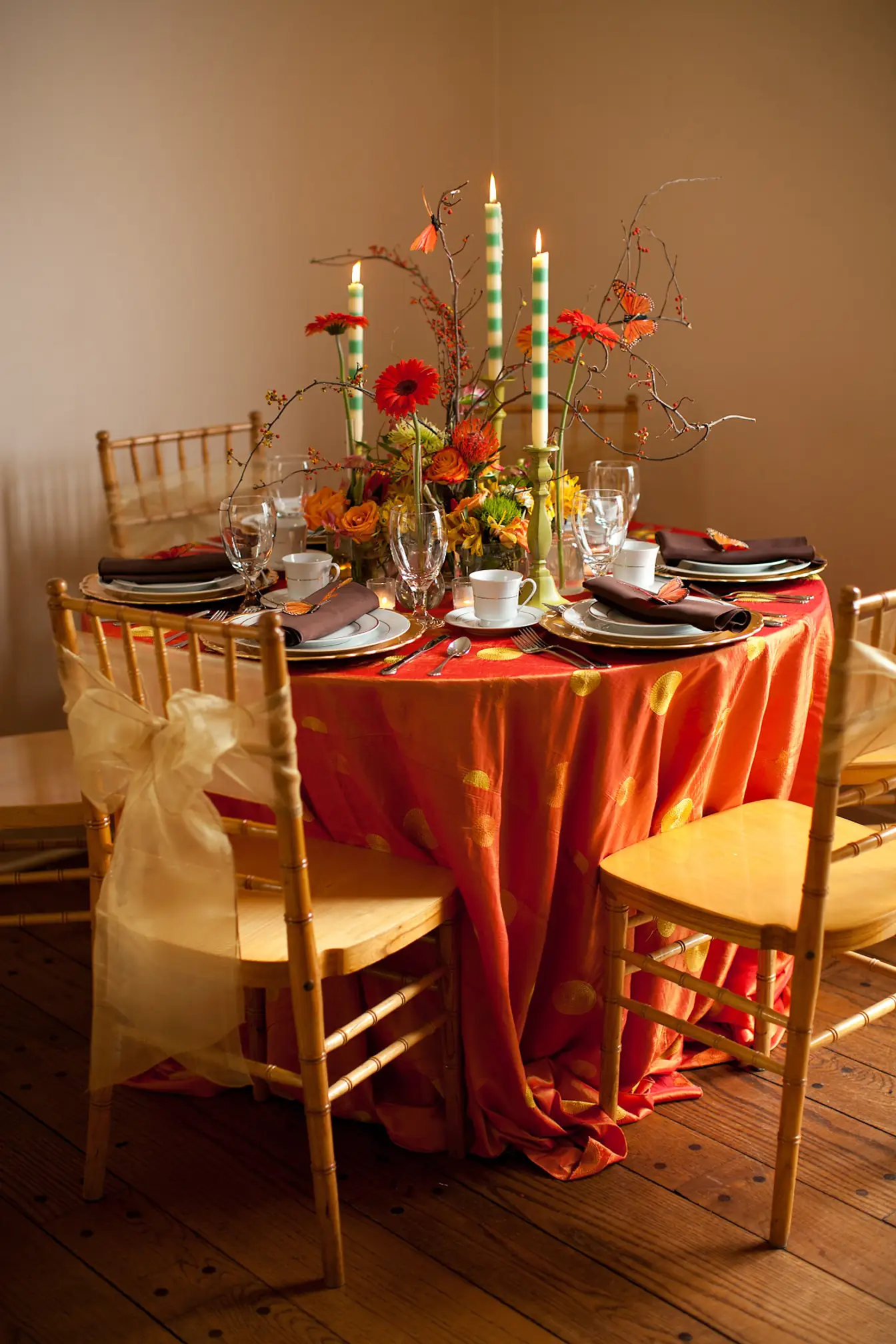 Orange satin linens with sheer sash and gold Chiavari chairs, set with tea cups