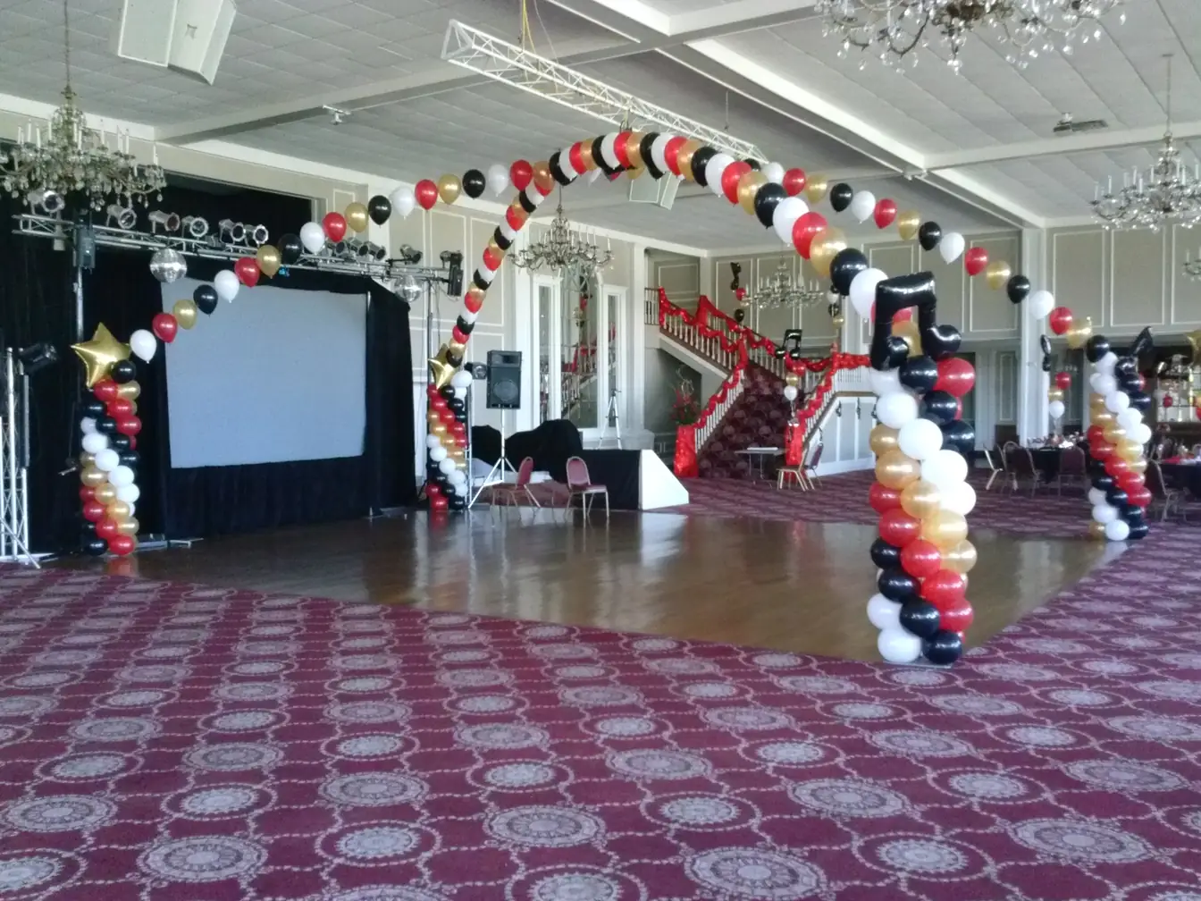 Prom room with black and pink balloon arches, red carpet, and covered chairs