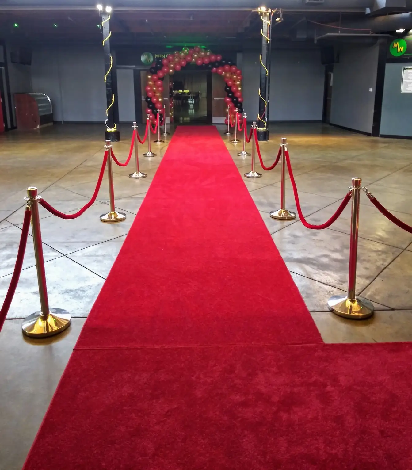 Long red carpet runner lined with gold stanchions and red velvet ropes leading to the doors of an event hall