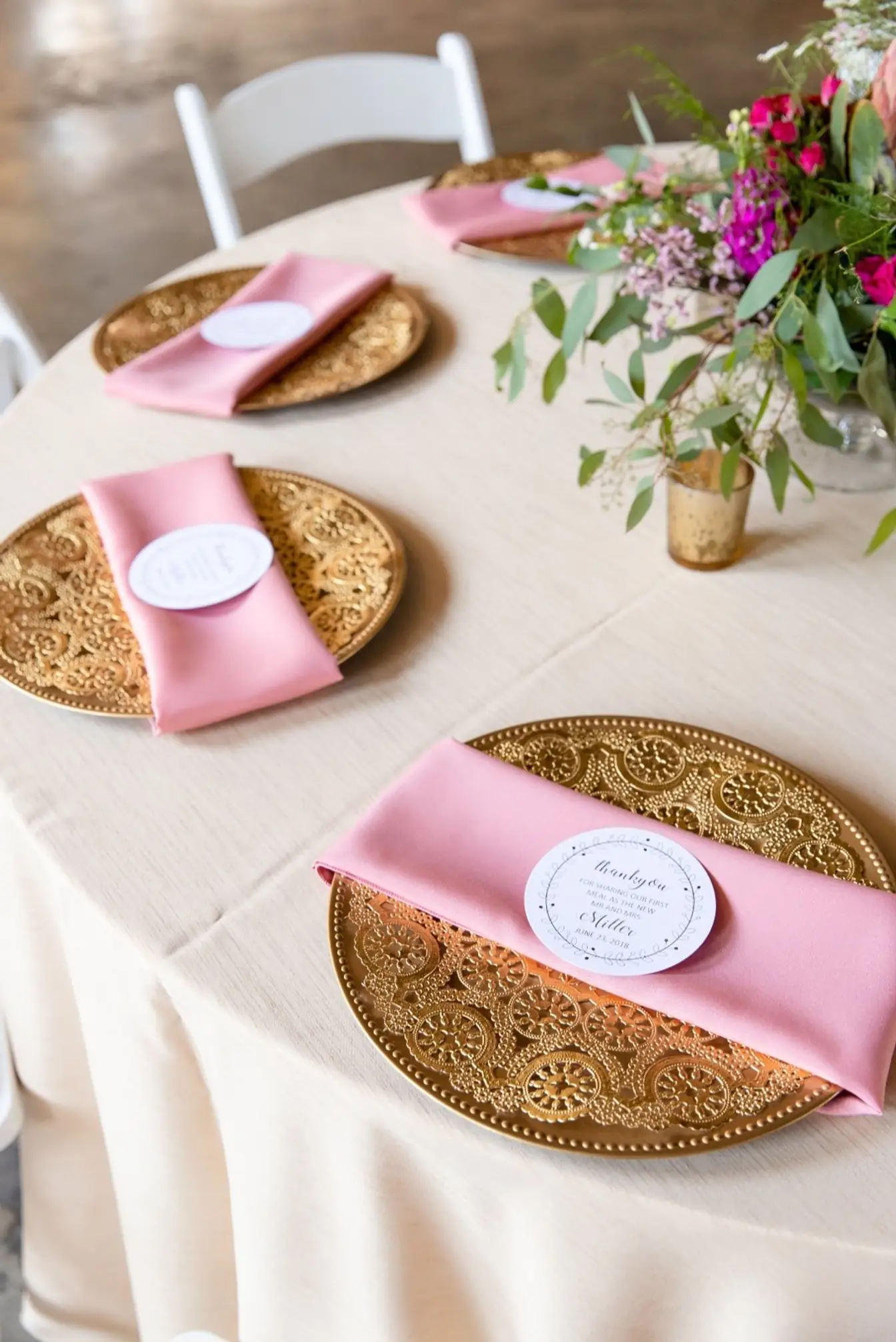 Gold lace charger plates layered with pink napkins and round thank-you cards on a champagne crinkle linen