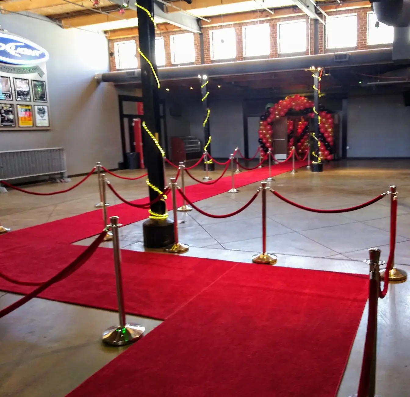 Red carpet runners crossing an industrial venue floor, lined with gold stanchions and red velvet ropes