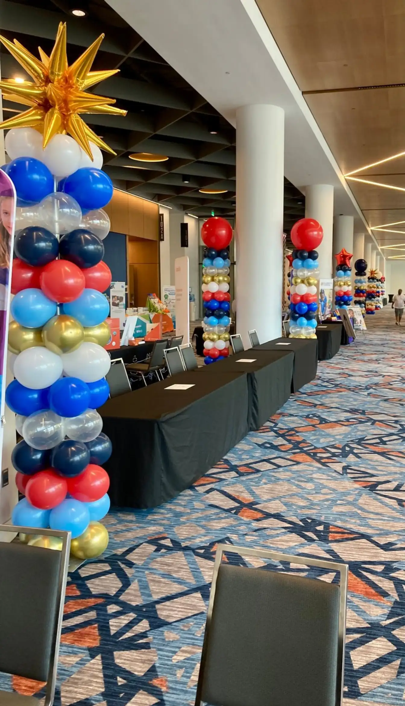Convention corridor with black-draped registration tables and star-topped balloon columns in red, white, blue, and gold