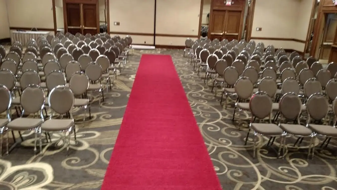 Red carpet aisle running between rows of banquet chairs in a hotel ballroom