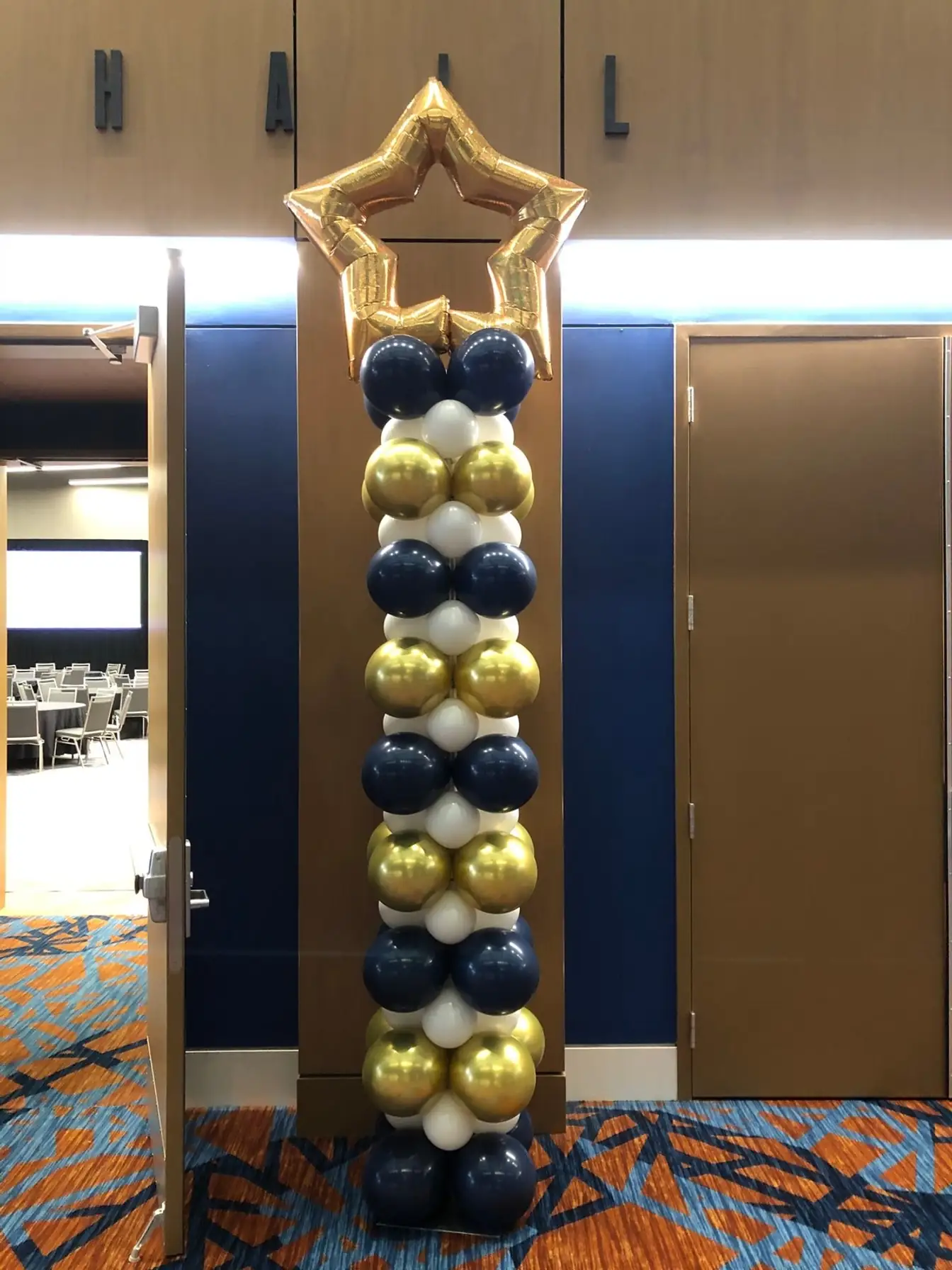 Navy, gold, and white balloon column topped with a gold star balloon beside a meeting hall doorway