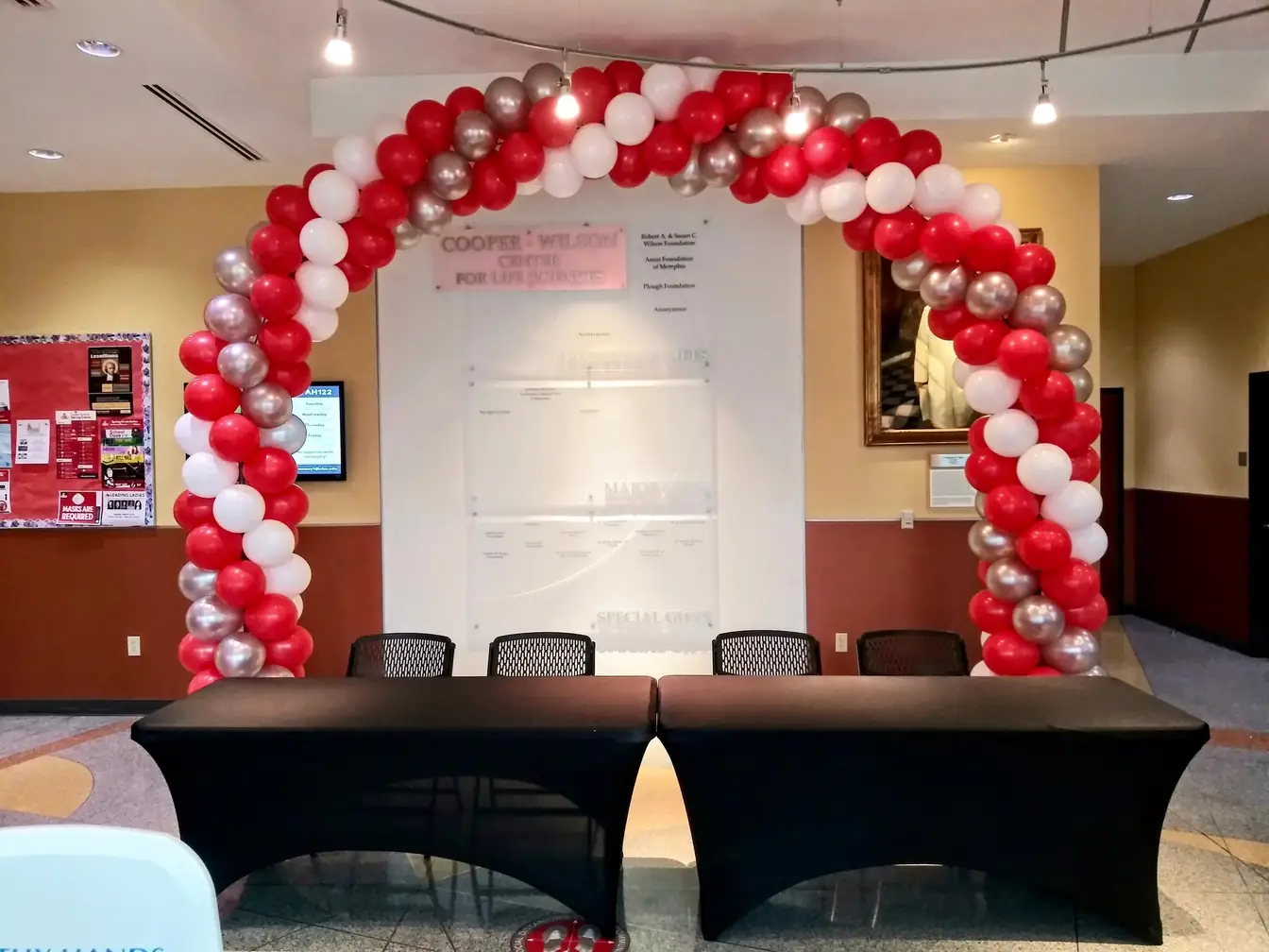 Red and white spiral balloon arch over a black-draped registration table in a corporate lobby