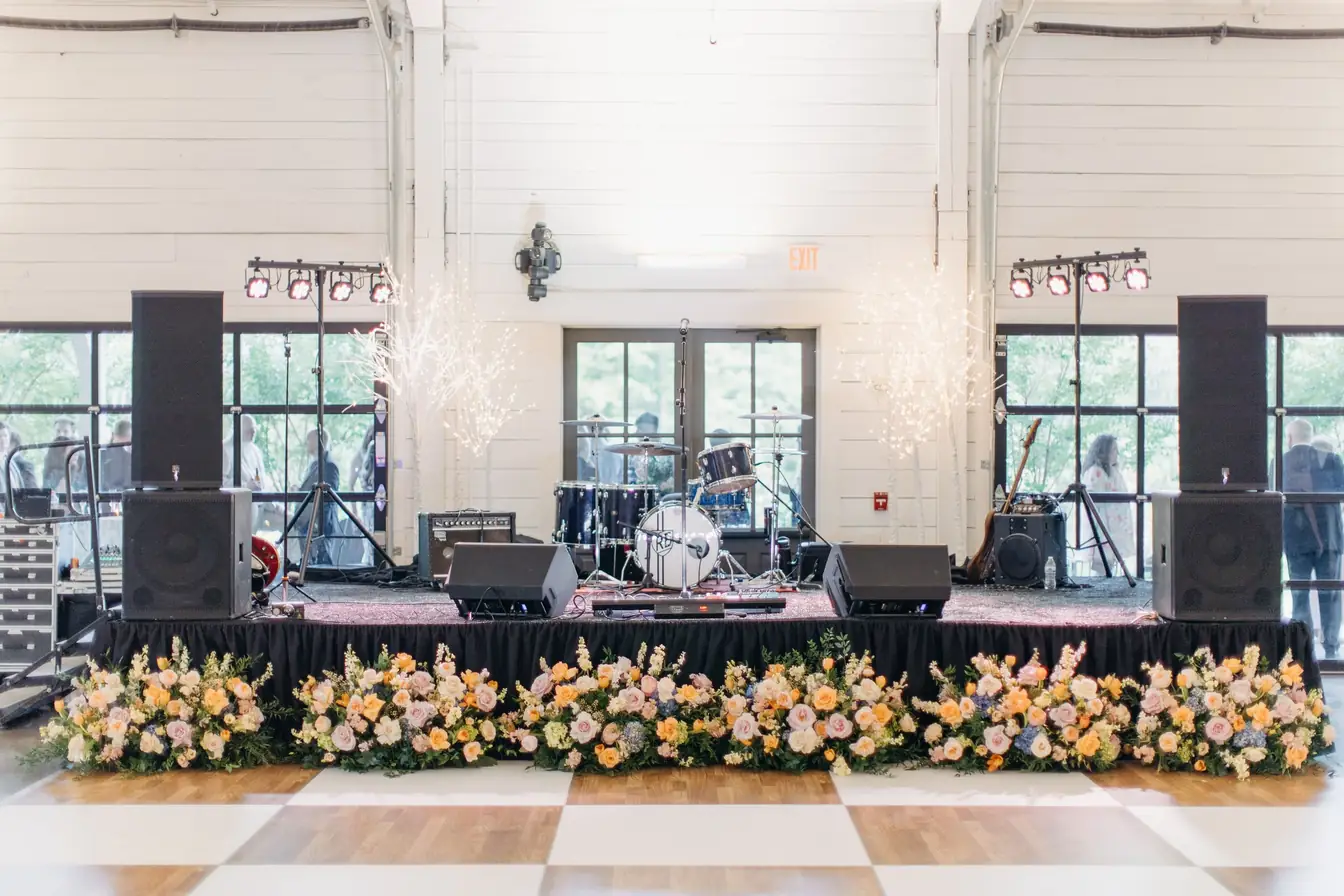 Band setup behind a black and white checkerboard dance floor edged with pastel floral garland