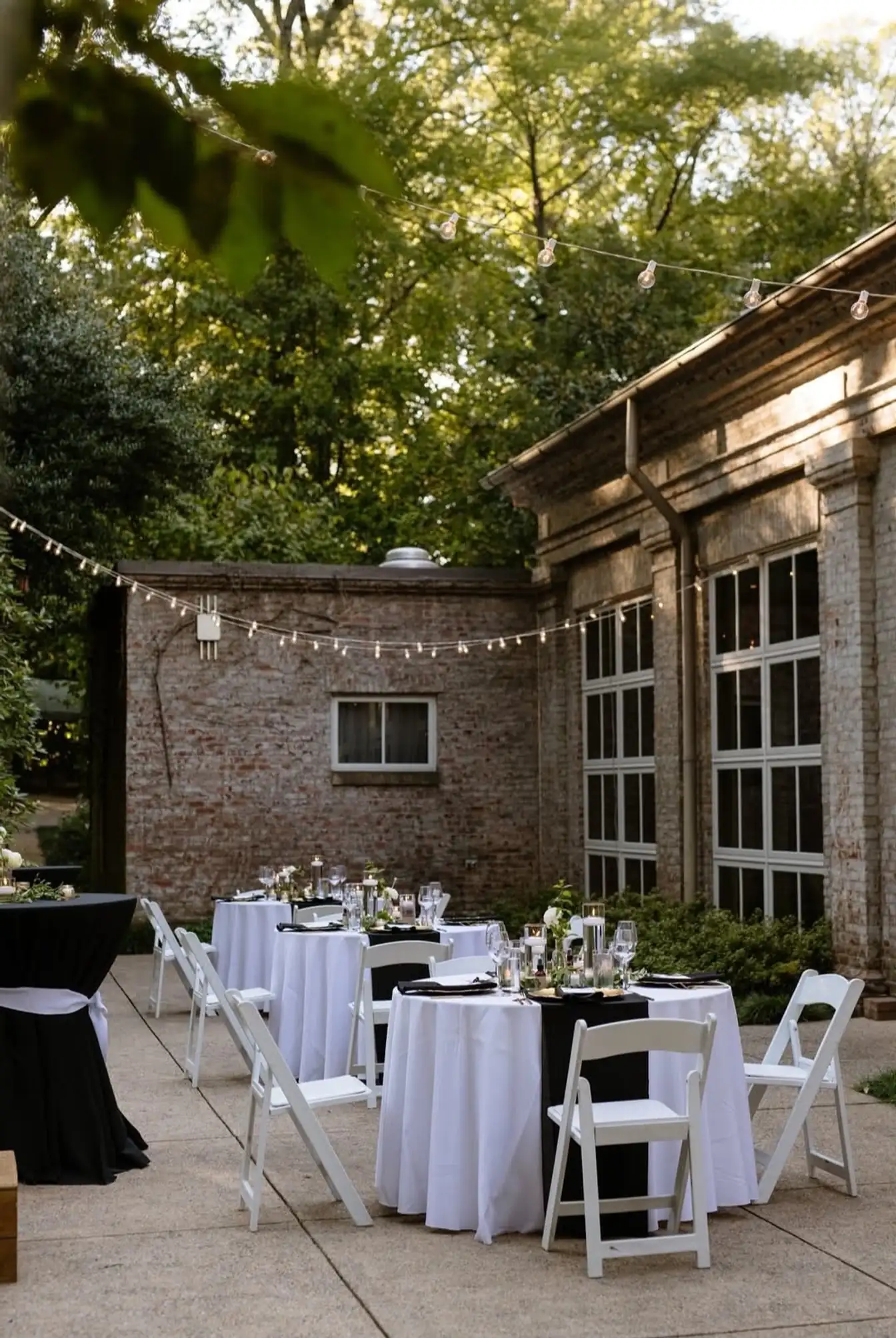 Courtyard reception with white-linen rounds, black cocktail tables and white folding chairs under bistro lights