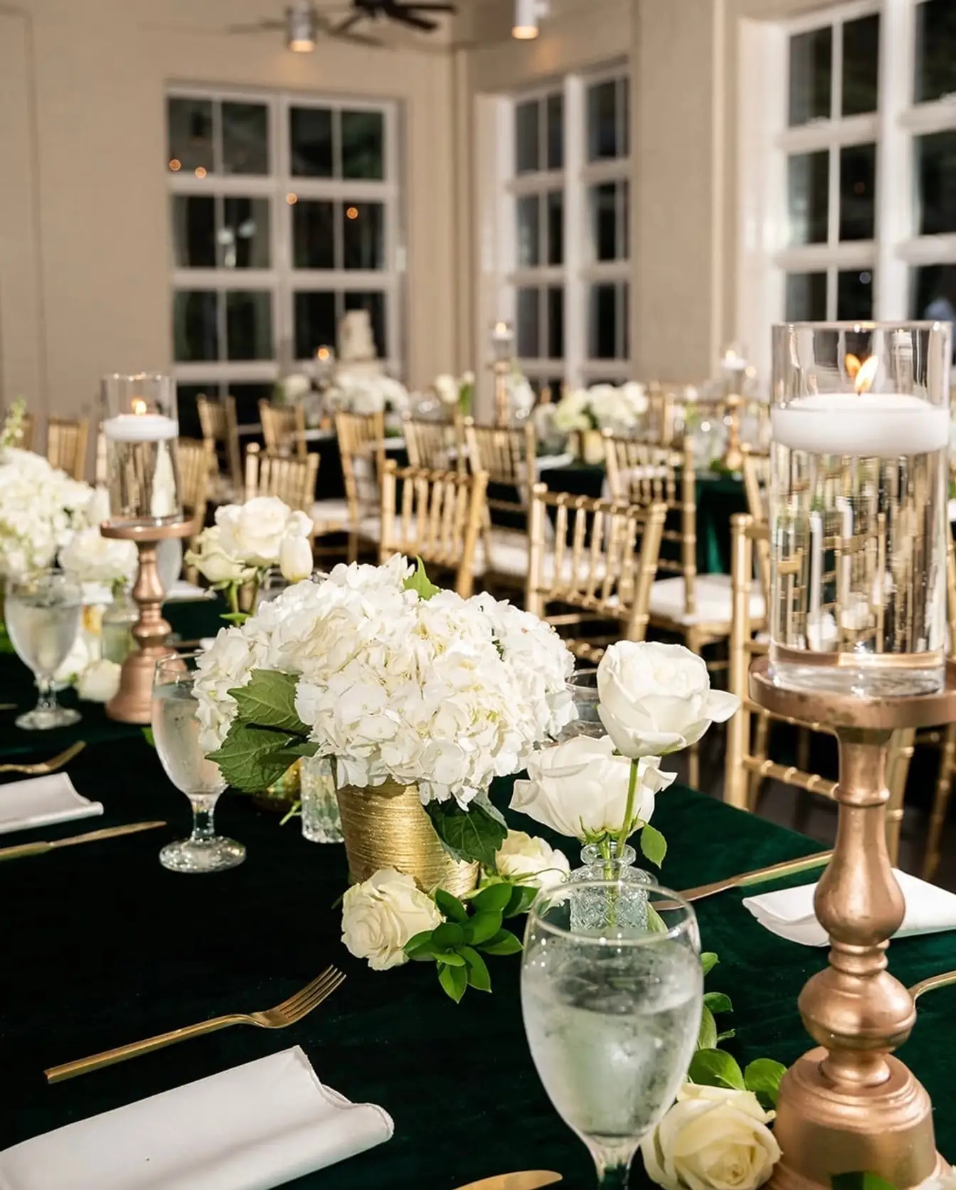 Hunter green linen with gold candlesticks, white hydrangea and rose centerpieces and gold Chiavari chairs