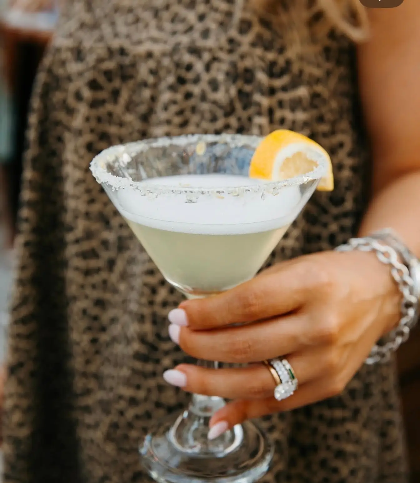 Salt-rimmed margarita glass with a lemon twist held at a party