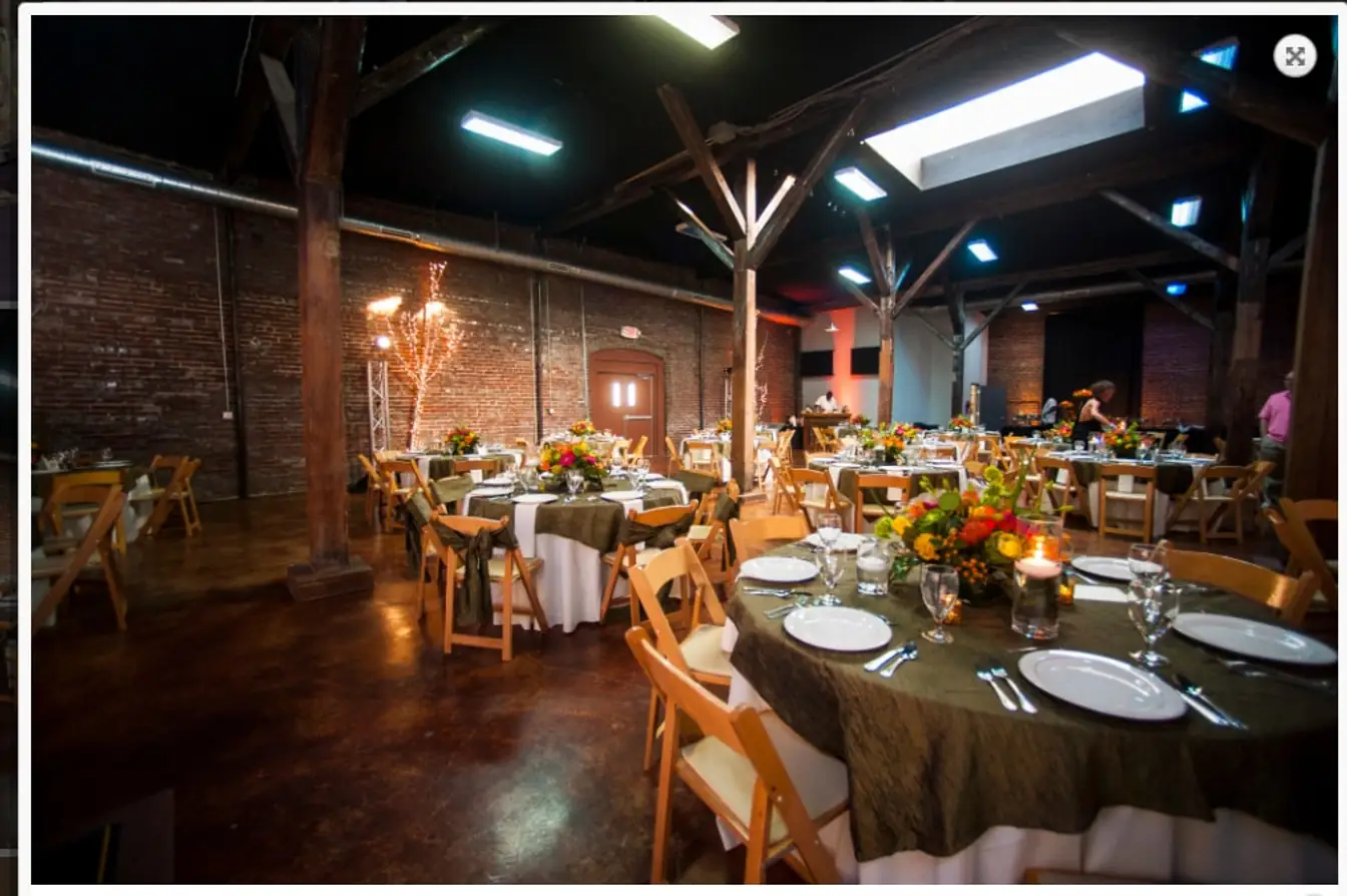Moss krinkle tablecloths on long tables with wood chairs and autumn florals in a brick warehouse