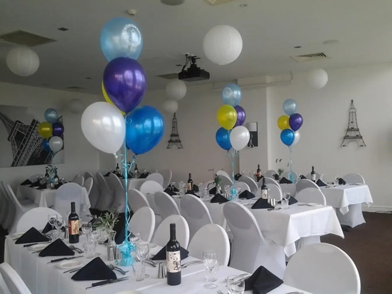 Balloon bouquets in blue, purple, white and gold weighted to white-linen tables at a Paris-themed party