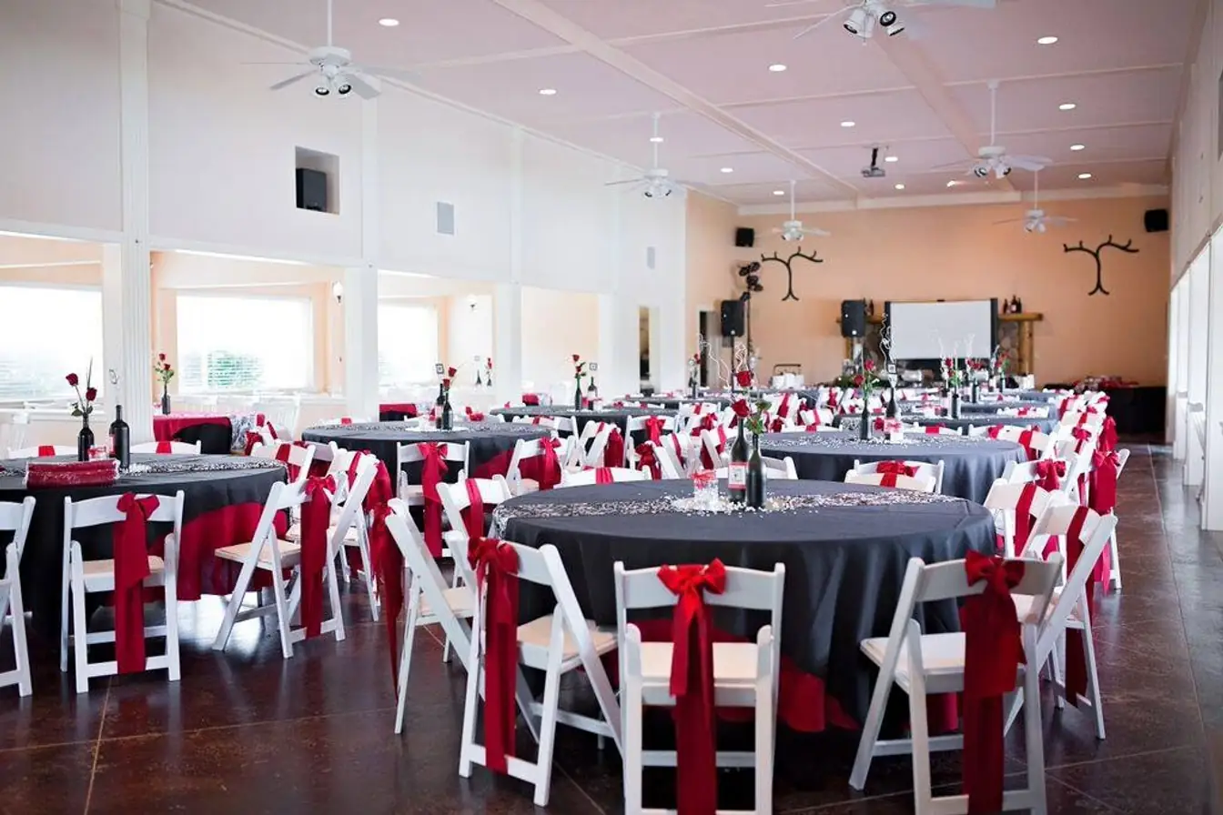 Red satin sashes tied on white chair covers at round tables set with white linens