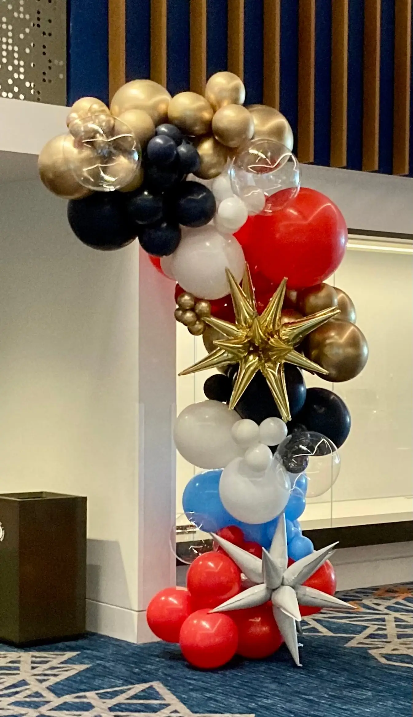 Organic balloon cluster in navy, gold, silver and red with star balloons beside a hotel lobby wall