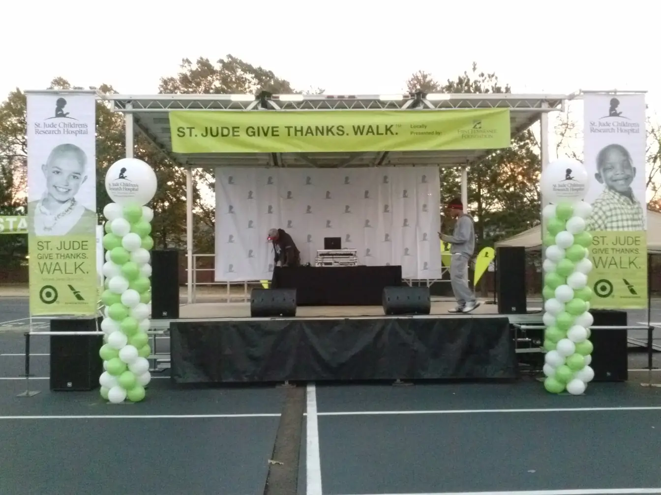 Green and white balloon columns flanking an outdoor event platform at a charity walk