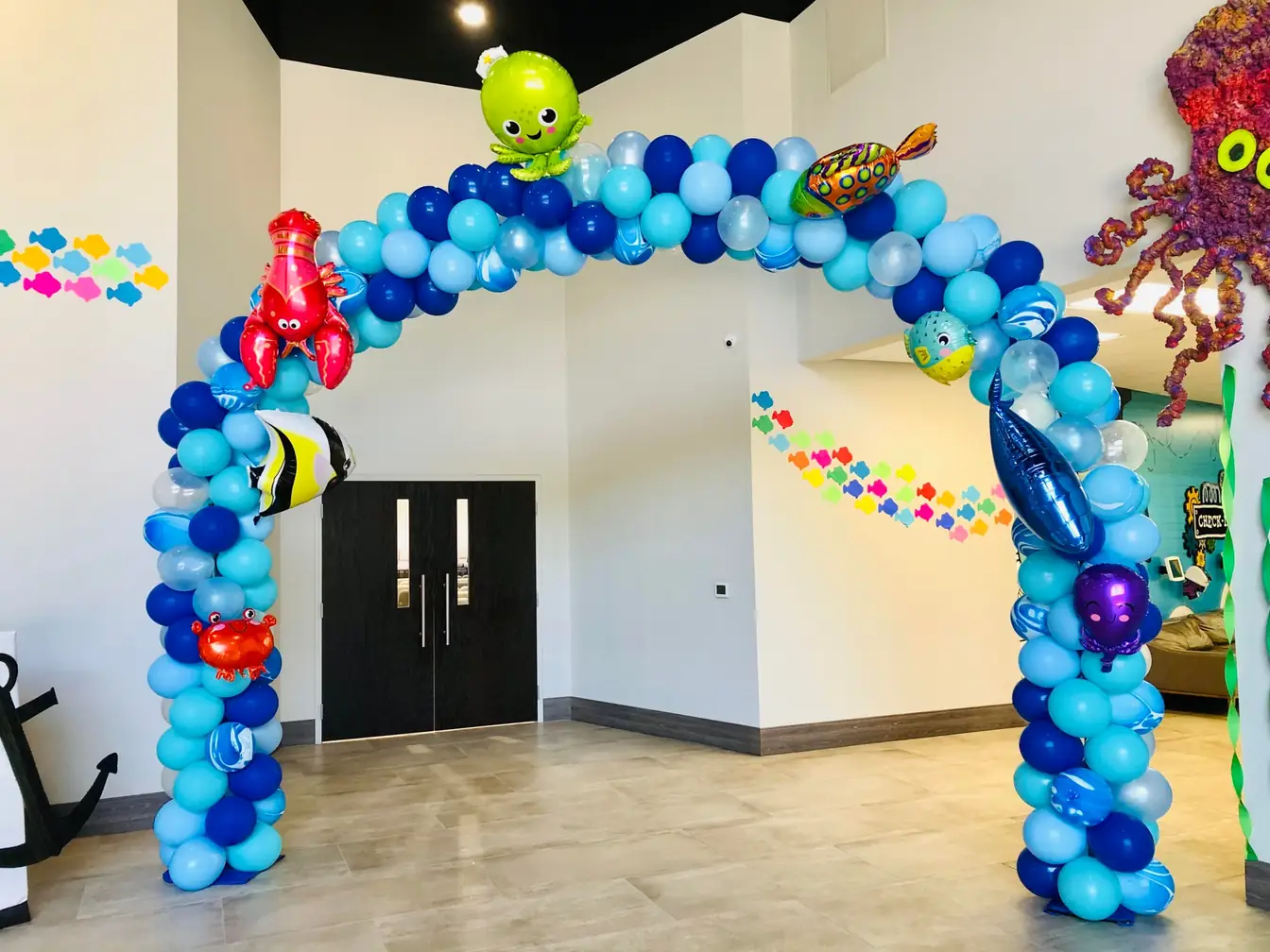 Blue and green spiral balloon arch with cartoon-character balloons in a bright hall