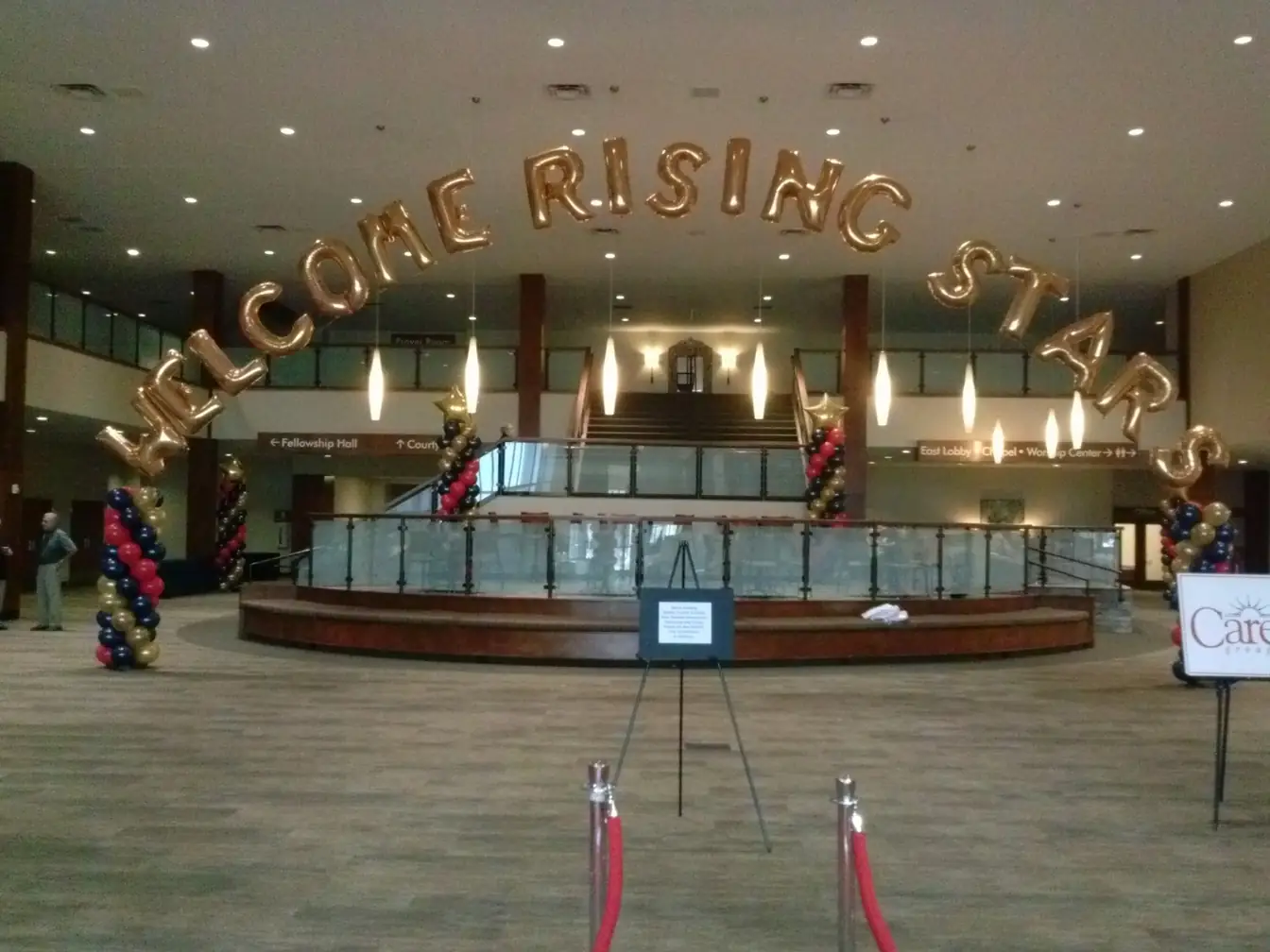 Gold balloon letters spelling Welcome Rising Stars over an arch of white, gold and black balloons