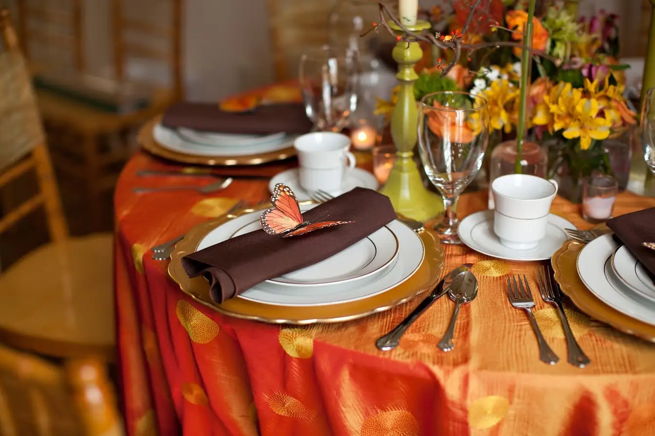 Round table in a burnt-orange embroidered tablecloth set with gold charger plates, gold-band china, chocolate napkins, and polished flatware